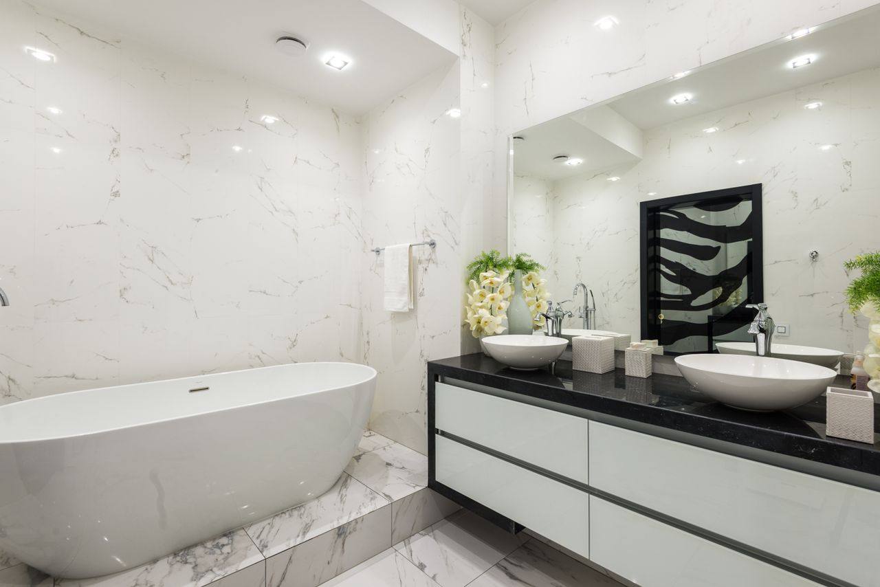 Interior of contemporary bathroom with white marble bathtub tiled walls and floor and cabinet under sink with chrome faucet